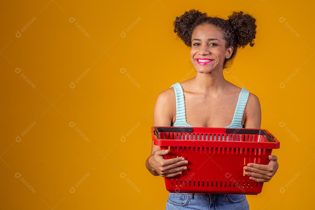 Jovem Afro Mulher sorridente segurando cesta de compras vazia