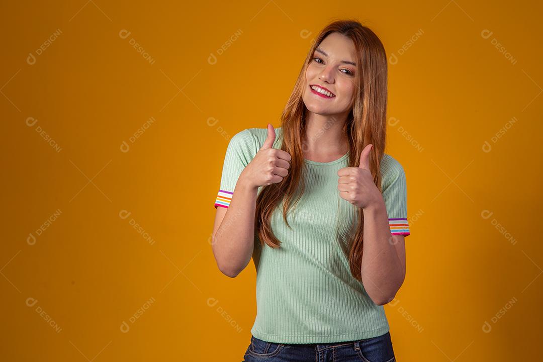 Jovem Ruiva Sorrindo Olhando para a Câmera e fazendo sinal de Jóia