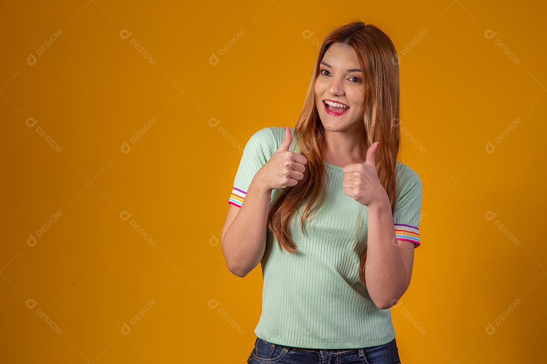 Jovem Ruiva Sorrindo Olhando para a Câmera e fazendo sinal de Jóia