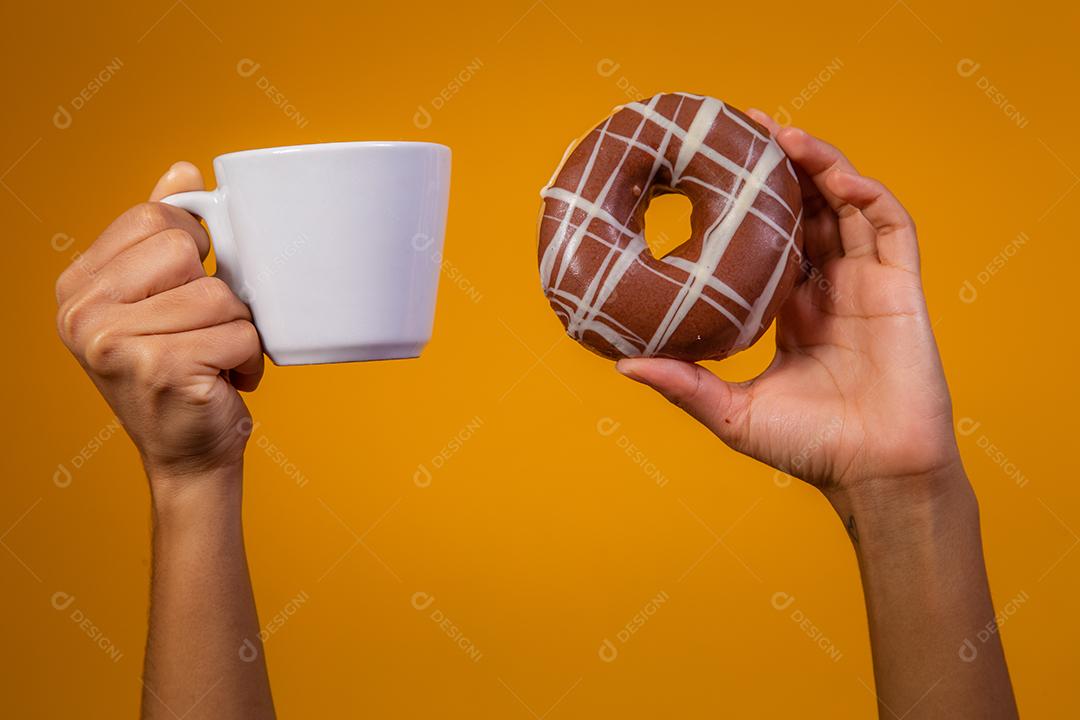 Mão segurando copo de leite e rosquinhas
