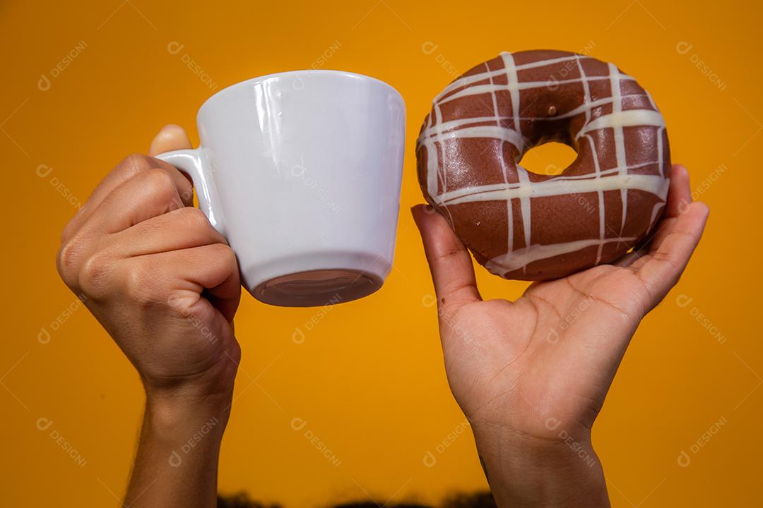Mão segurando copo de leite e rosquinhas