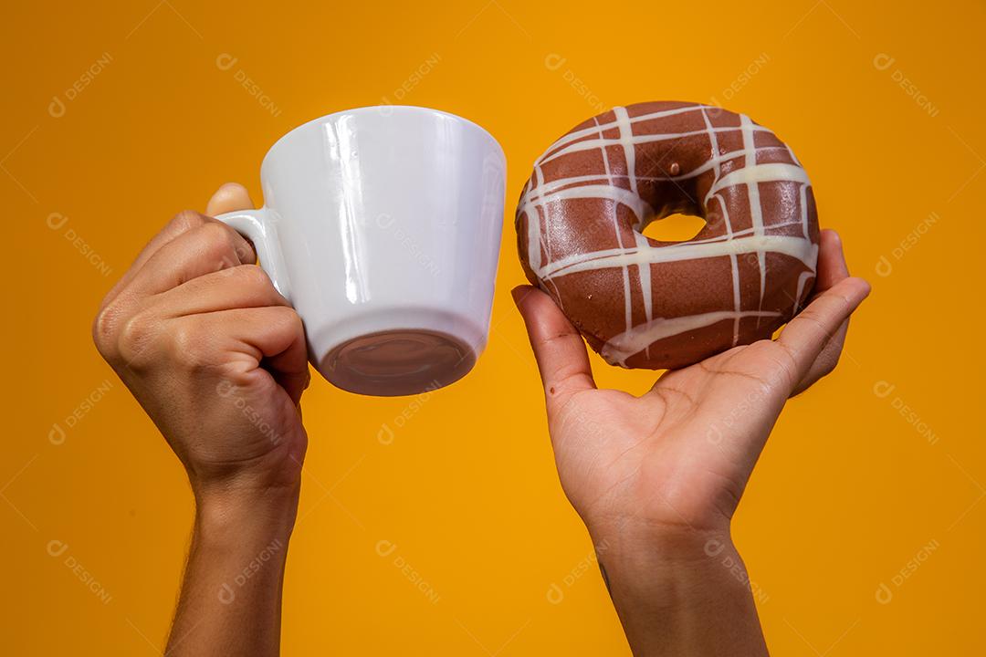 Mão segurando copo de leite e rosquinhas