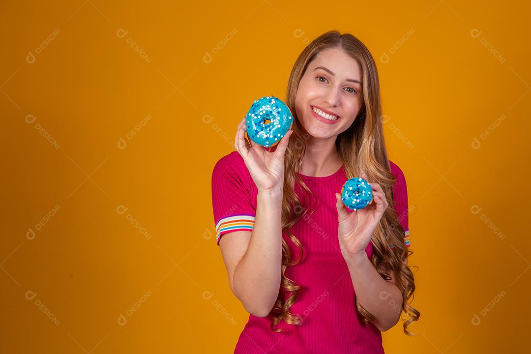 Retrato de uma menina bonita alegre segurando rosquinhas azuis no rosto