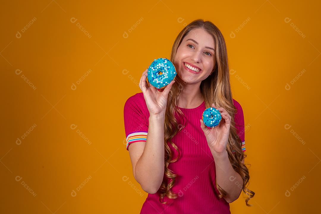 Retrato de uma menina bonita alegre segurando rosquinhas azuis no rosto