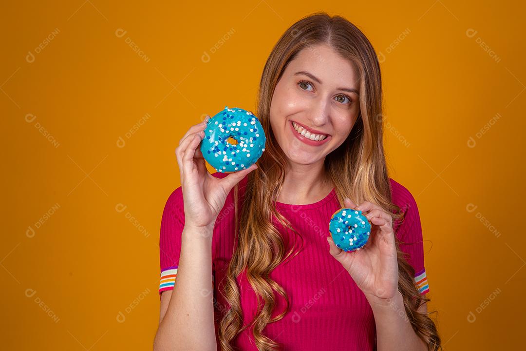 Retrato de uma menina bonita alegre segurando rosquinhas azuis no rosto