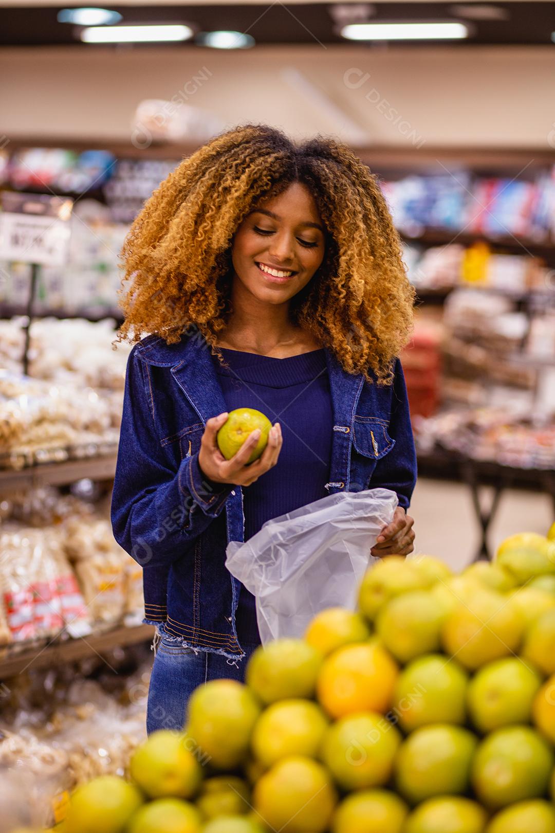 Jovem afro fazendo compras no supermercado hortifruti empurrando carrinho de compras