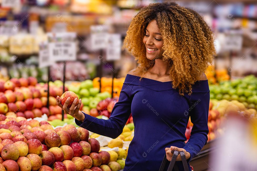Jovem afro fazendo compras no supermercado hortifruti empurrando carrinho de compras