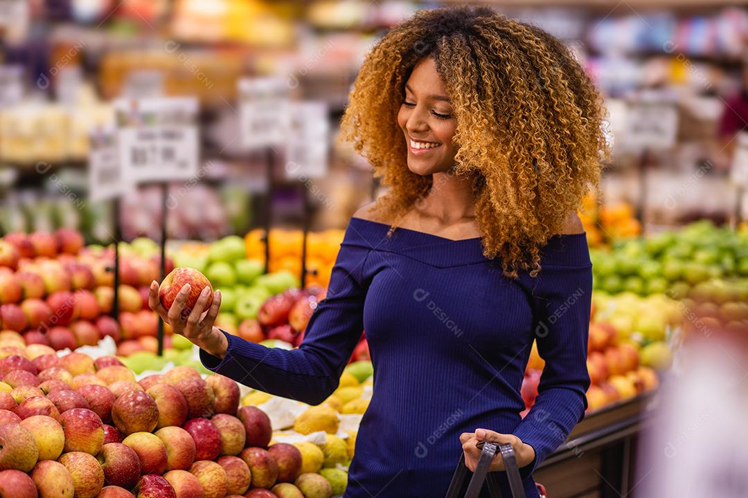 Jovem afro fazendo compras no supermercado hortifruti empurrando carrinho de compras