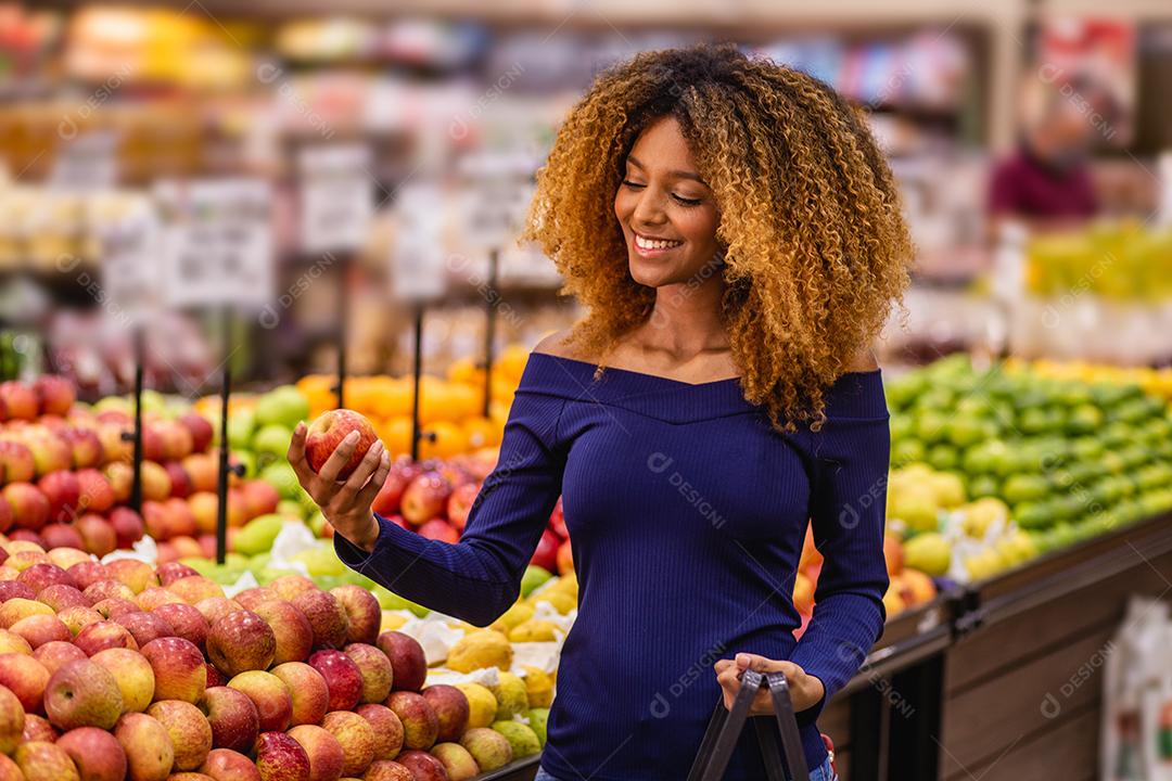 Jovem afro fazendo compras no supermercado hortifruti empurrando carrinho de compras