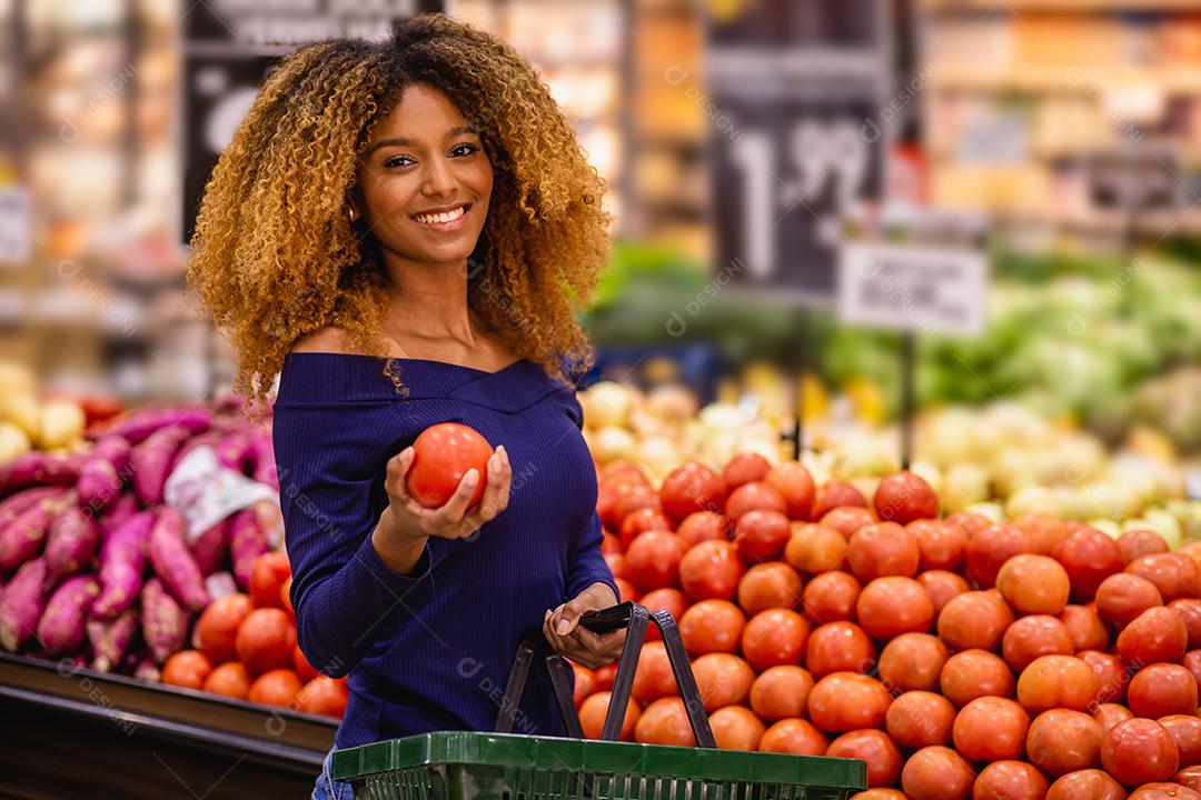 Jovem afro fazendo compras no supermercado hortifruti empurrando carrinho de compras