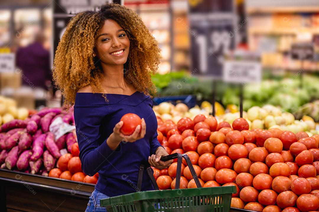 Jovem afro fazendo compras no supermercado hortifruti empurrando carrinho de compras