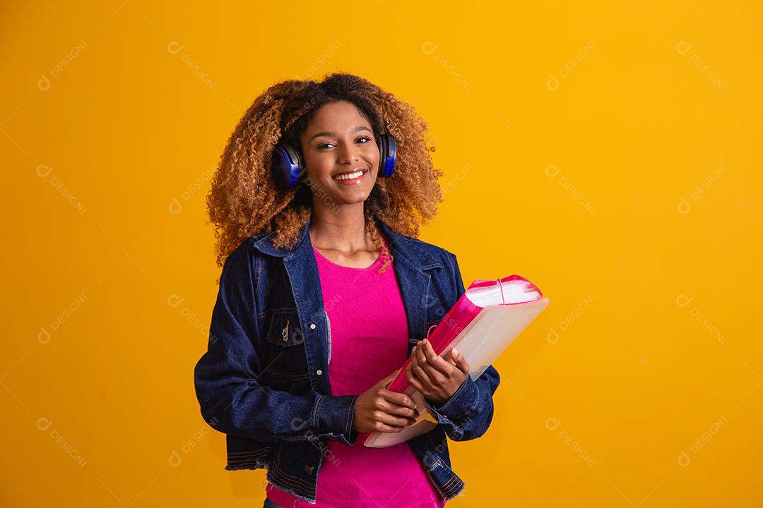 jovem estudante afro com livros sobre fundo amarelo.