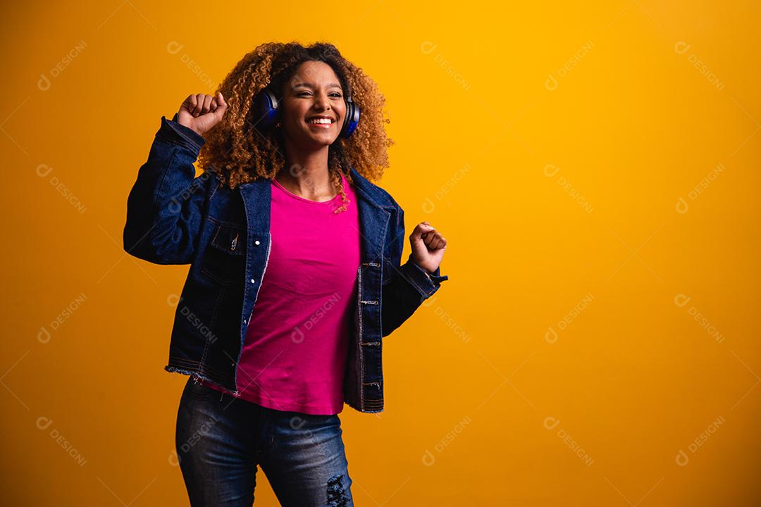 Mulher jovem e bonita com cabelo afro, ouvindo música com o fone de ouvido sorrindo.