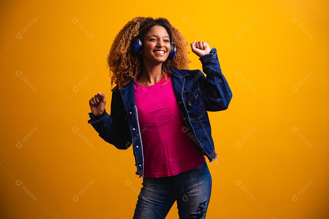 Mulher jovem e bonita com cabelo afro, ouvindo música com o fone de ouvido sorrindo.