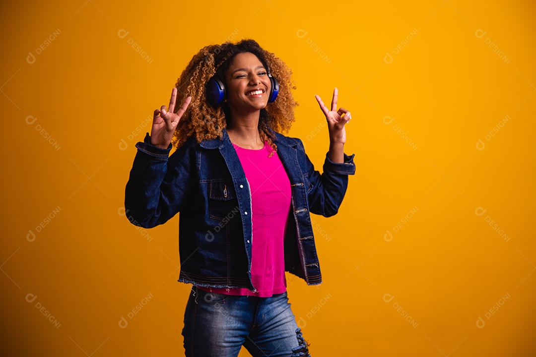 Mulher jovem e bonita com cabelo afro, ouvindo música com o fone de ouvido sorrindo.