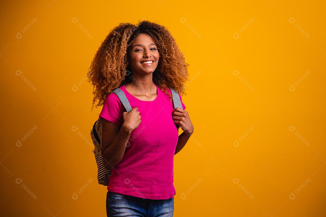 jovem afro com mochila nas costas em fundo amarelo. jovem estudante sorrindo