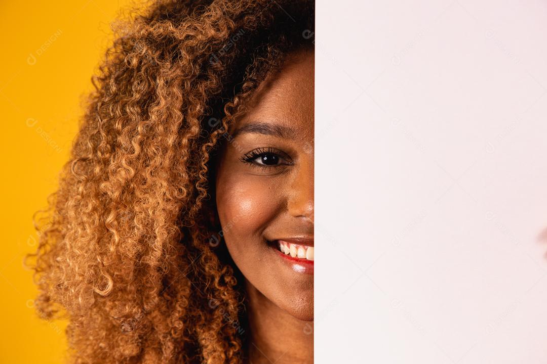 Mulher afro segurando Papel Branco a frete do rosto em fundo amarelo