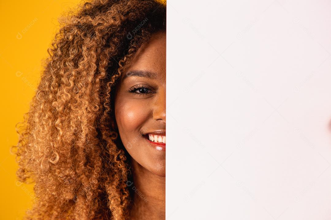 Mulher afro segurando Papel Branco a frete do rosto em fundo amarelo