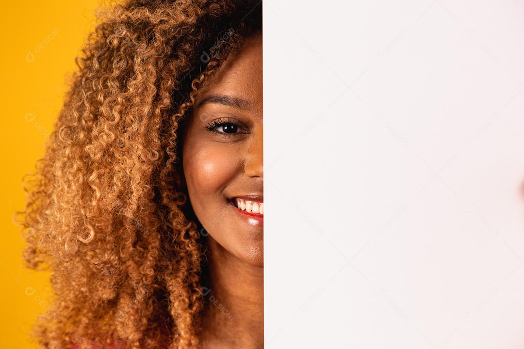 Mulher afro segurando Papel Branco a frete do rosto em fundo amarelo