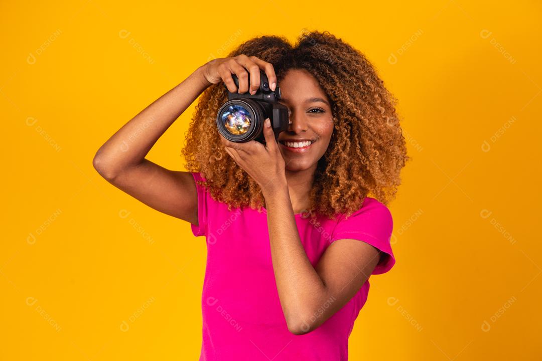 Mulher afro segurando câmera fotográfica em fundo amarelo