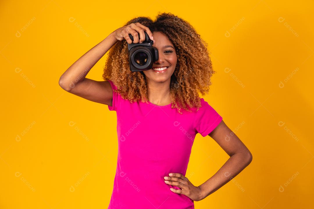 Mulher afro segurando câmera fotográfica em fundo amarelo