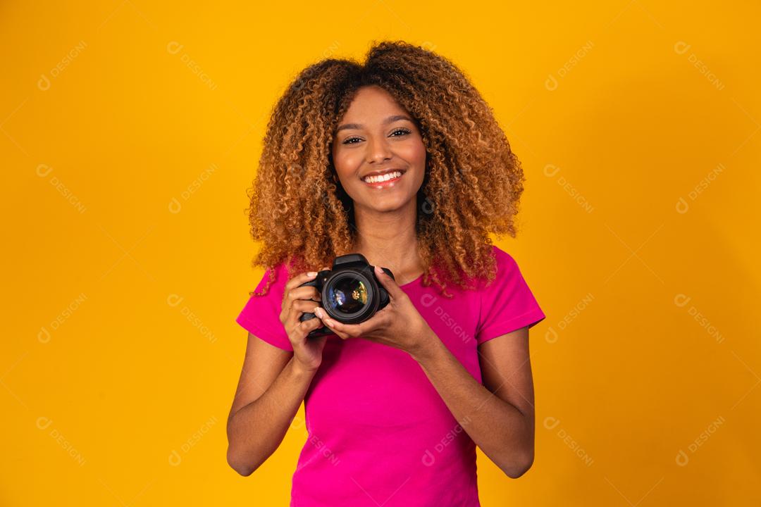 Mulher afro segurando câmera fotográfica em fundo amarelo