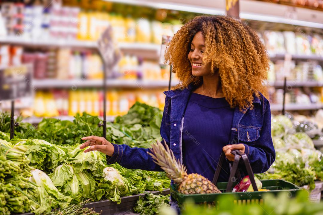 Jovem afro fazendo compras no supermercado hortifruti empurrando carrinho de compras