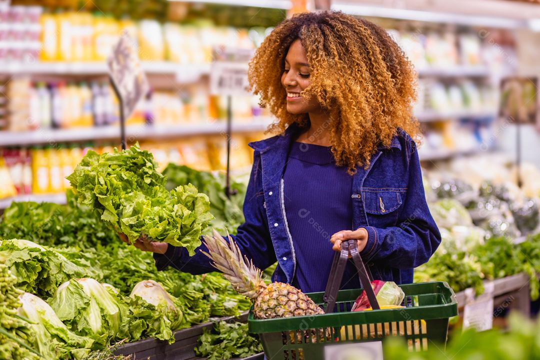 Jovem afro fazendo compras no supermercado hortifruti empurrando carrinho de compras