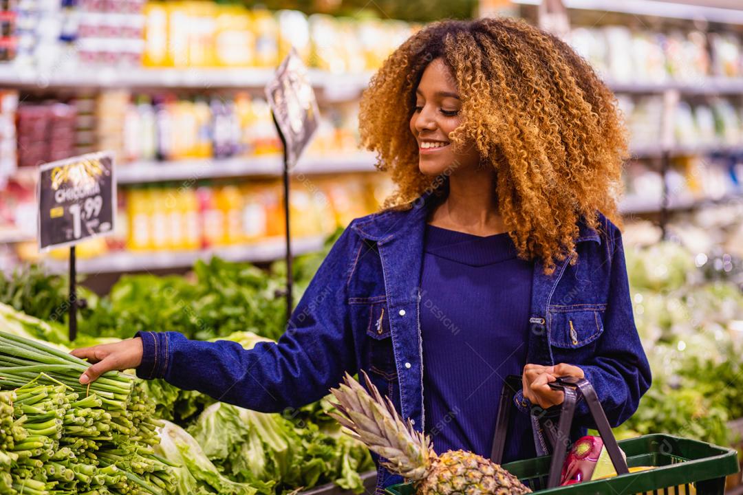 Jovem afro fazendo compras no supermercado hortifruti empurrando carrinho de compras