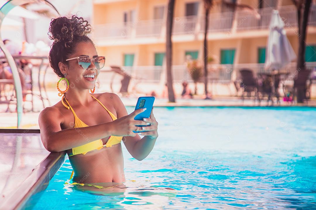 mulher trabalhando pelo celular na piscina do hotel