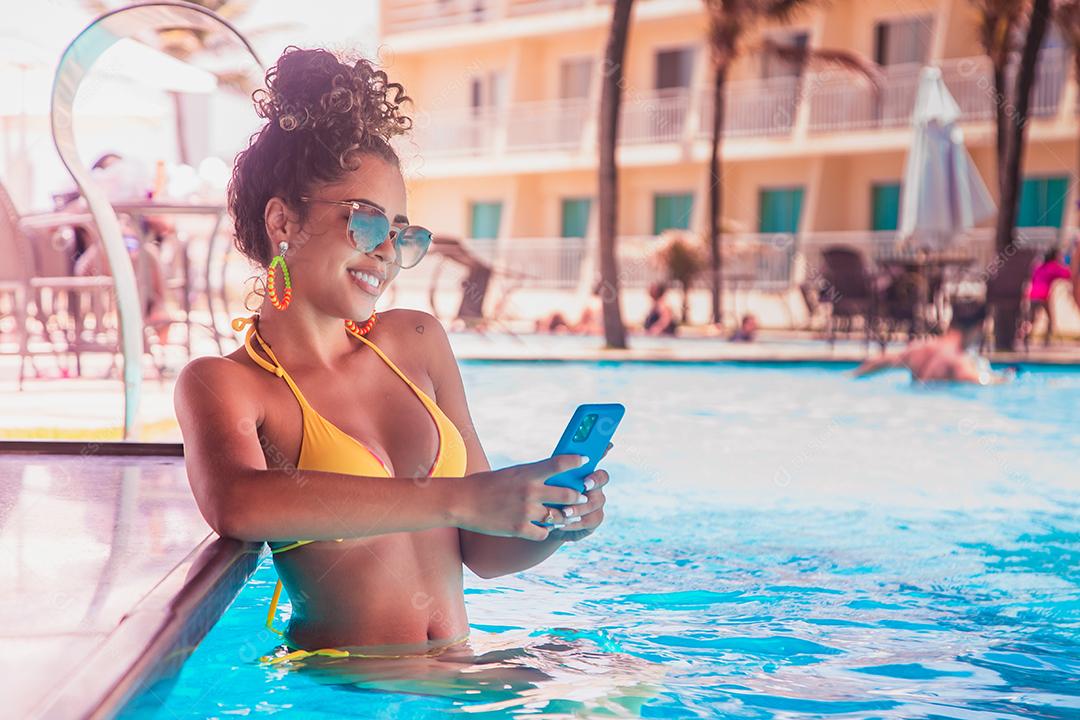 mulher trabalhando pelo celular na piscina do hotel