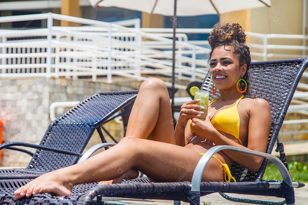 Mulher de biquini sentada em beira de piscina em hotel