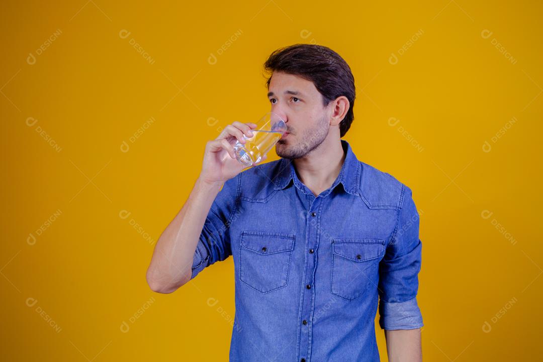 Homem com camisa jeans em fundo amarelo Bebendo água