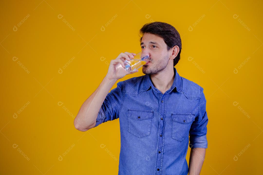 Homem com camisa jeans em fundo amarelo Bebendo água