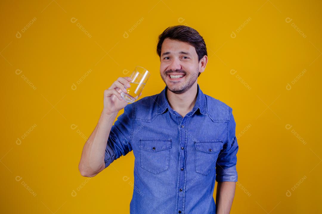 Homem com camisa jeans em fundo amarelo Bebendo água