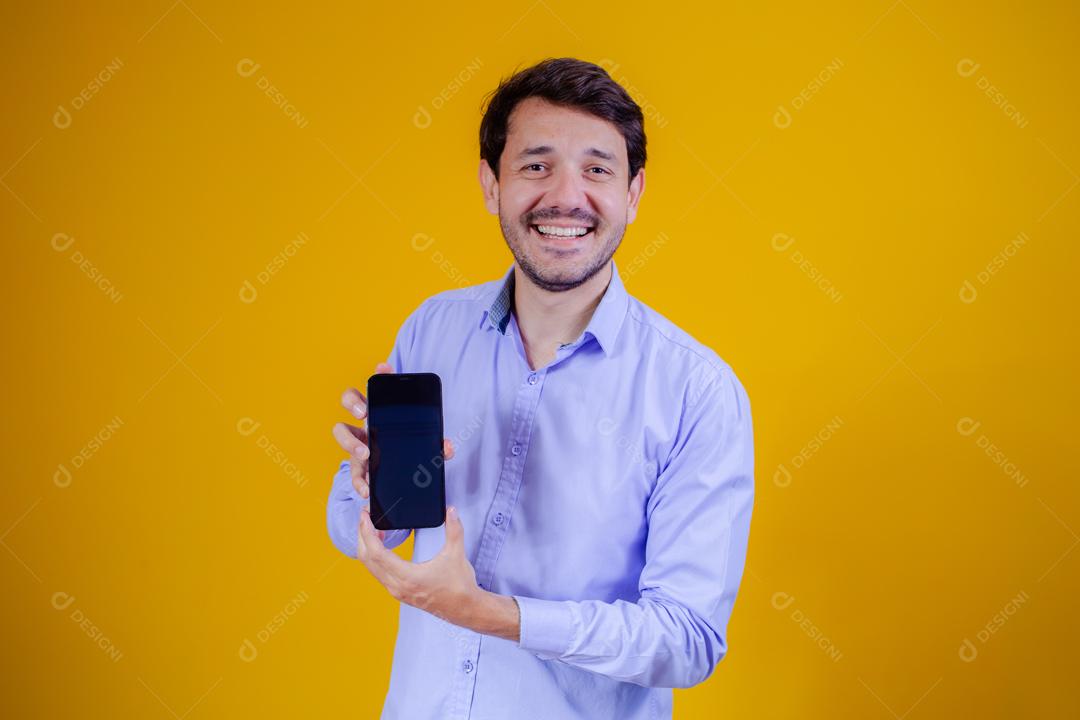 Homem com camisa social manga longa em fundo amarelo Apontando para celular