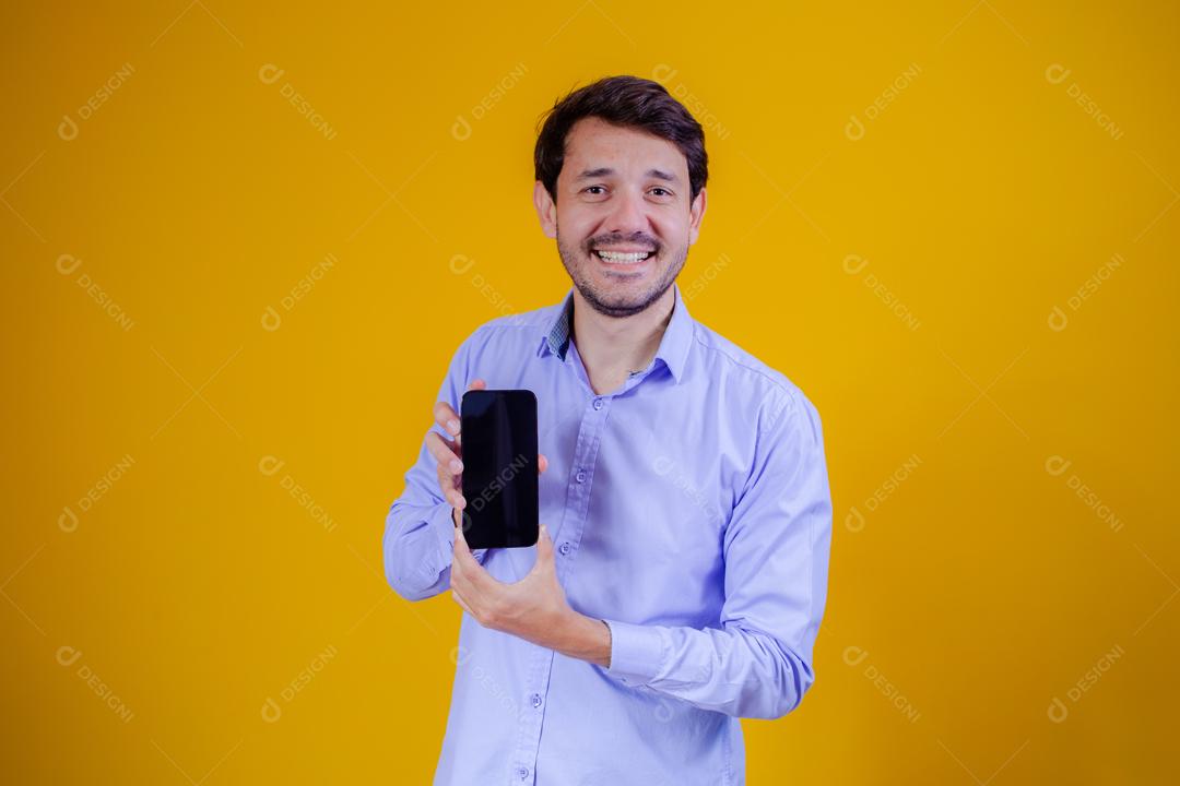 Homem com camisa social manga longa em fundo amarelo Apontando para celular