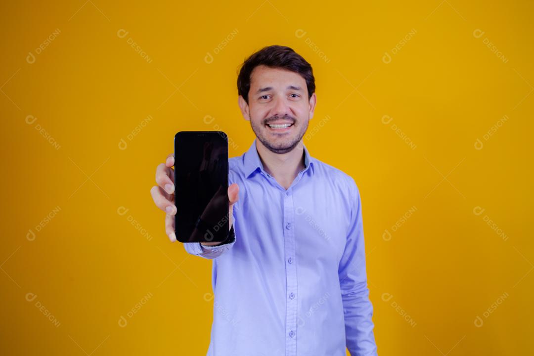 Homem com camisa social manga longa em fundo amarelo Apontando para celular