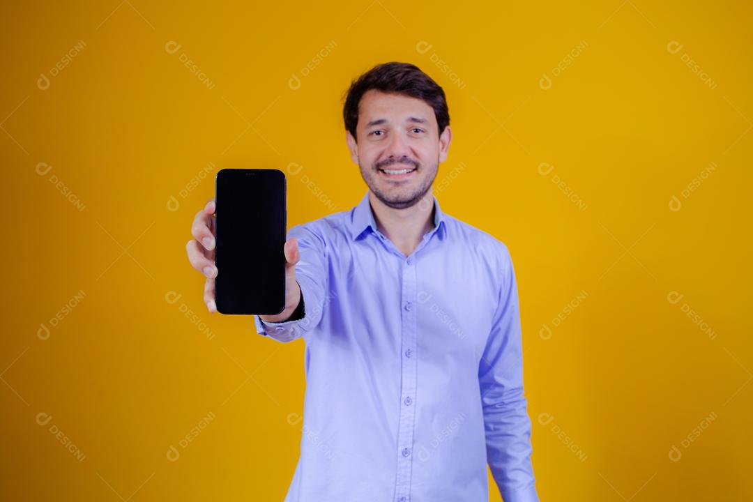 Homem com camisa social manga longa em fundo amarelo Apontando para celular