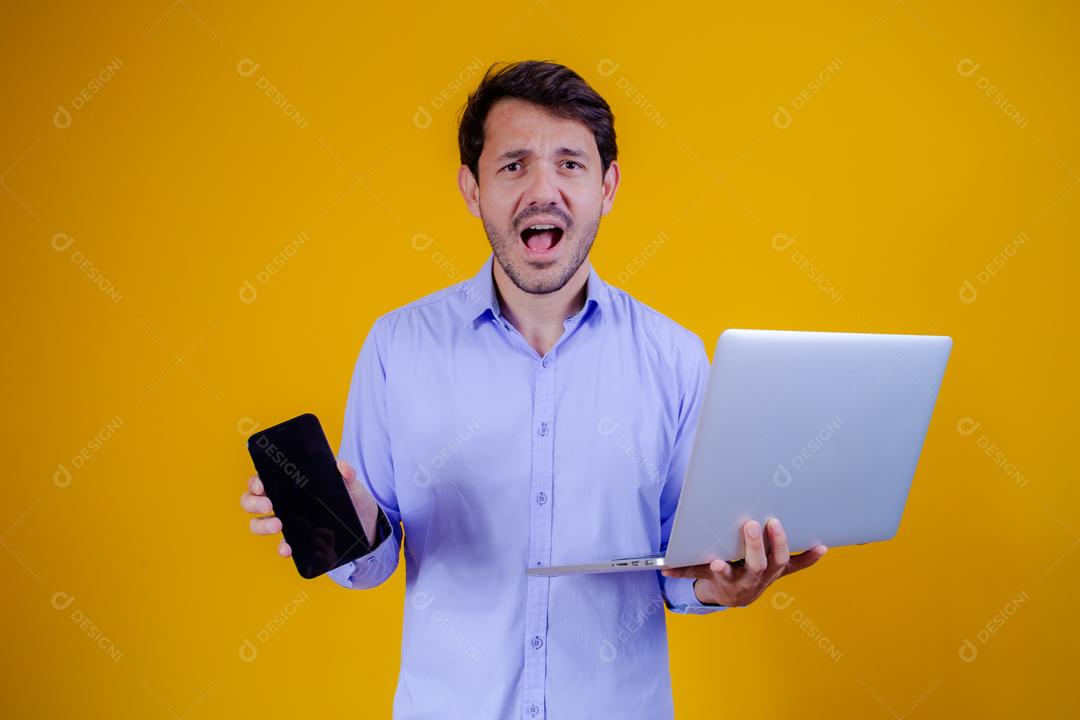 Homem com camisa social manga longa em fundo amarelo Segurando celular e Notebook e Computador