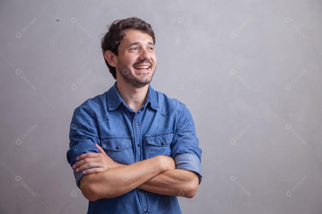 Homem  com roupa social camisa jeans e expressão de felicidade em fundo cinza