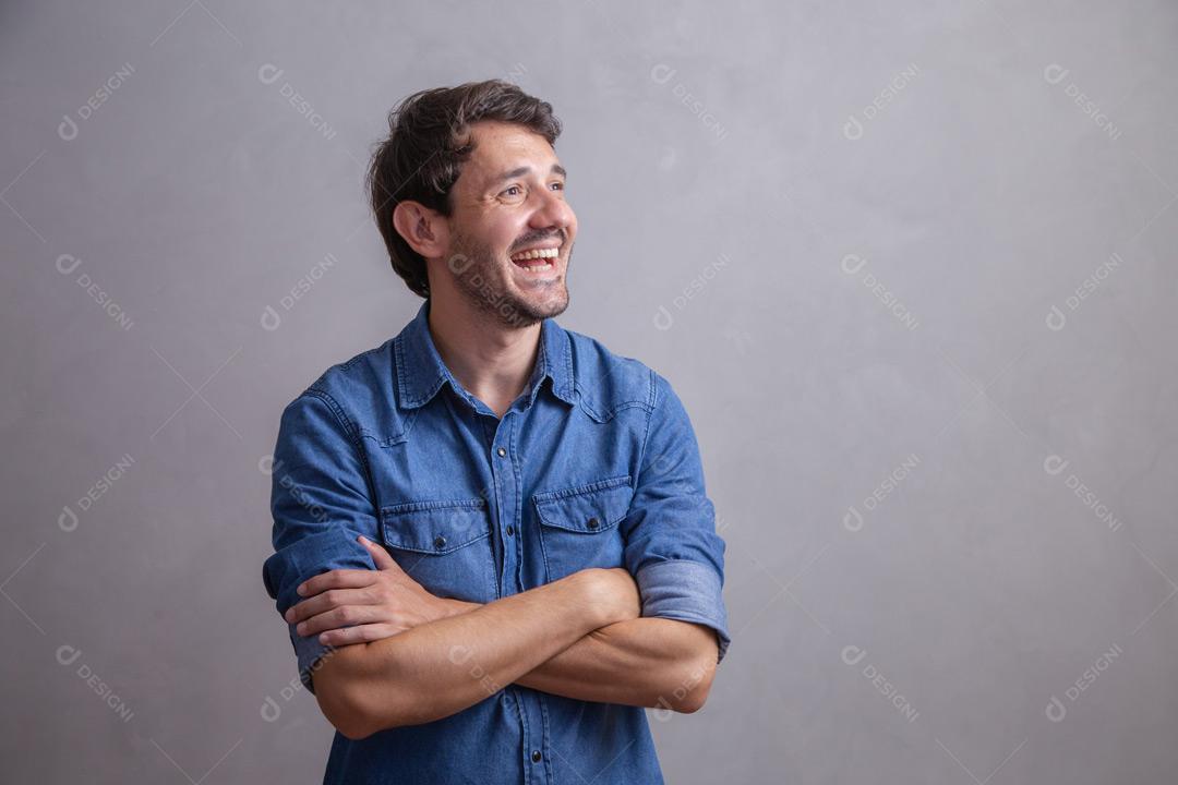 Homem  com roupa social camisa jeans e expressão de felicidade em fundo cinza