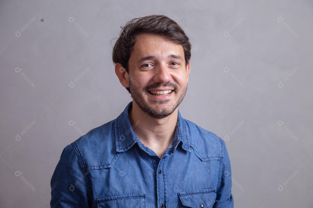 Homem  com roupa social camisa jeans e expressão de felicidade em fundo cinza