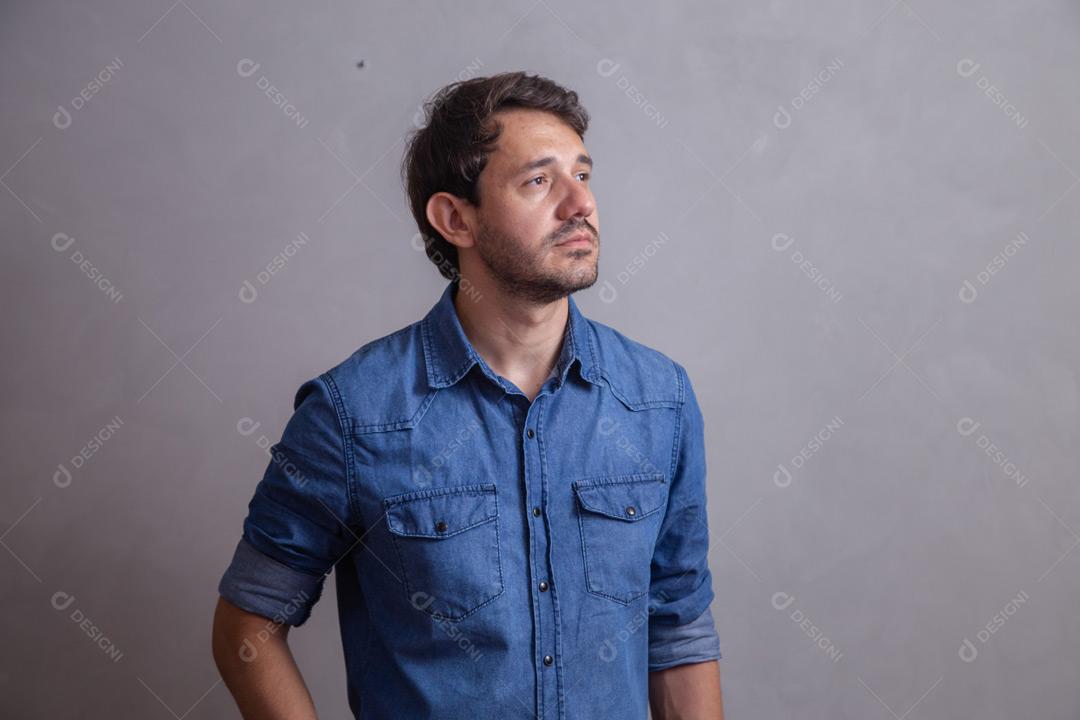 Homem  com roupa social camisa jeans e expressão de seria em fundo cinza