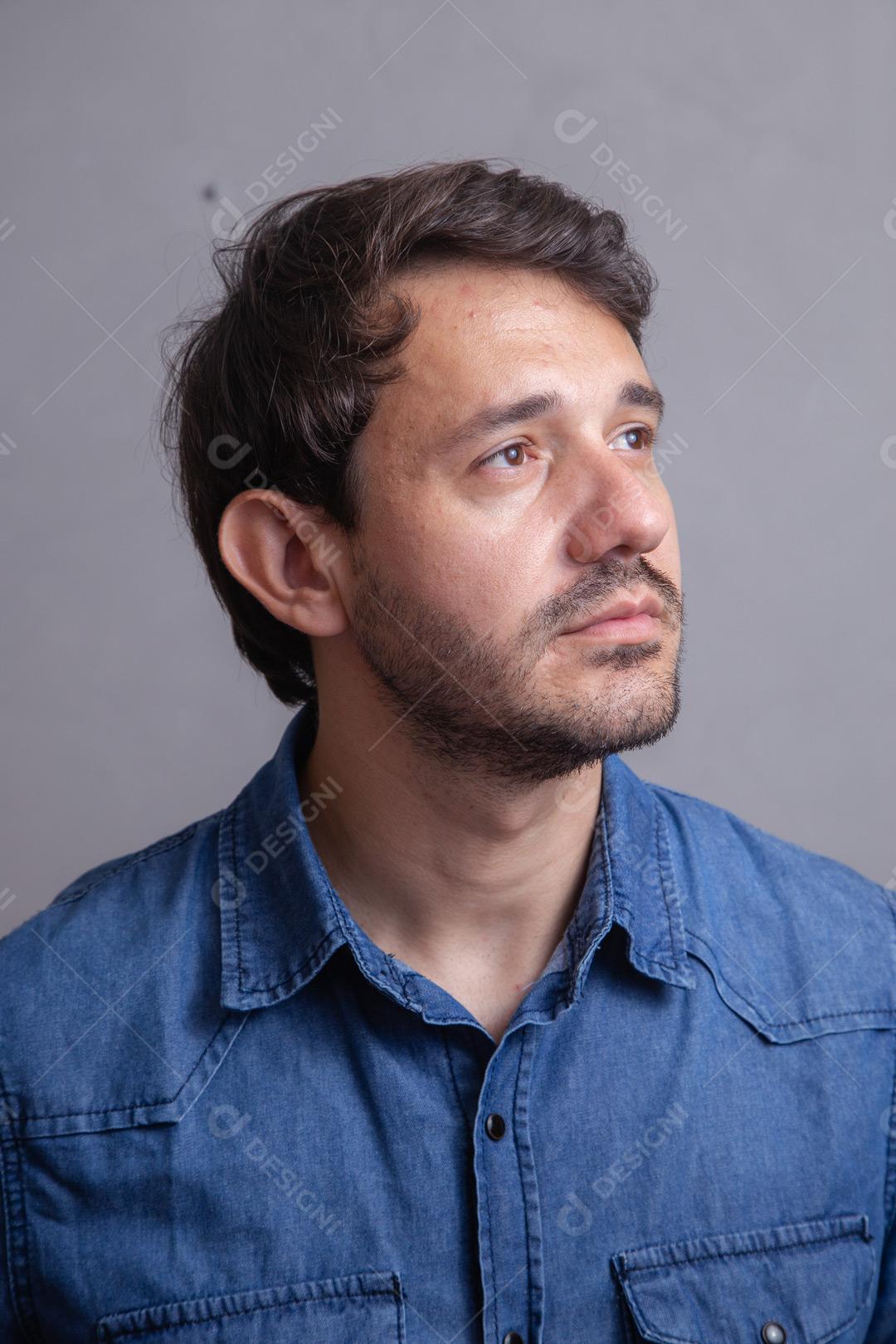 Homem  com roupa social camisa jeans e expressão de seria em fundo cinza