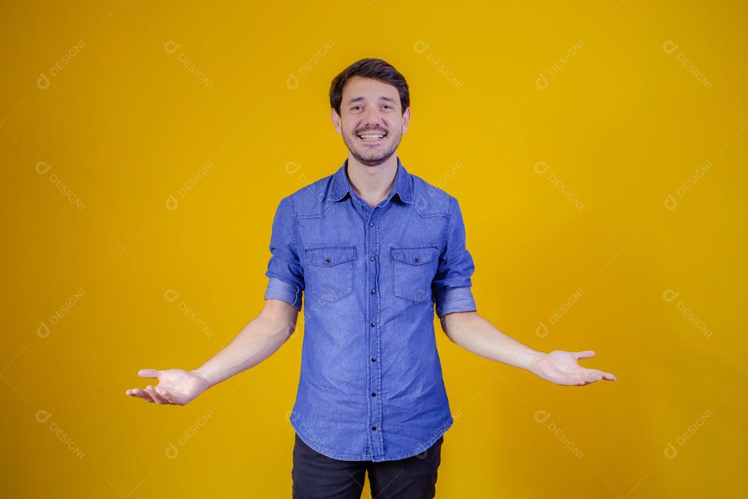 Homem com camisa jeans e braços abertos em fundo amarelo