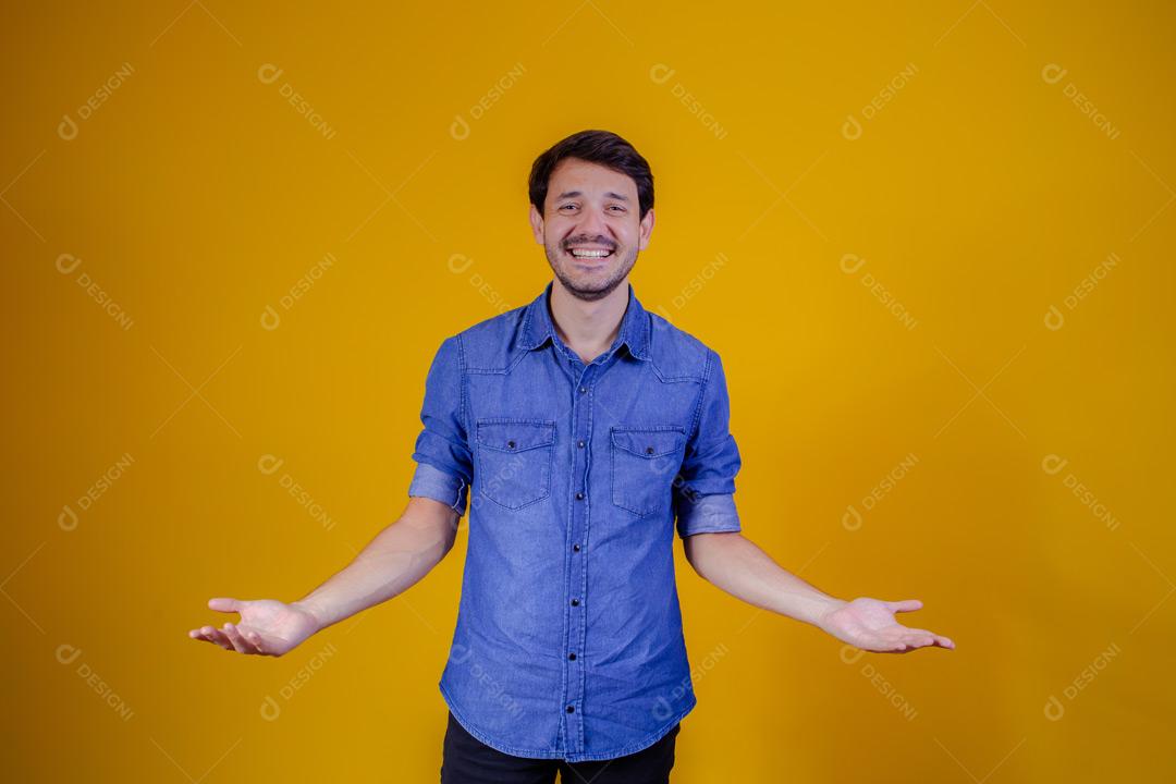 Homem com camisa jeans e braços abertos em fundo amarelo