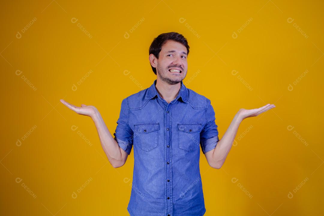 Homem com camisa jeans e braços abertos em fundo amarelo