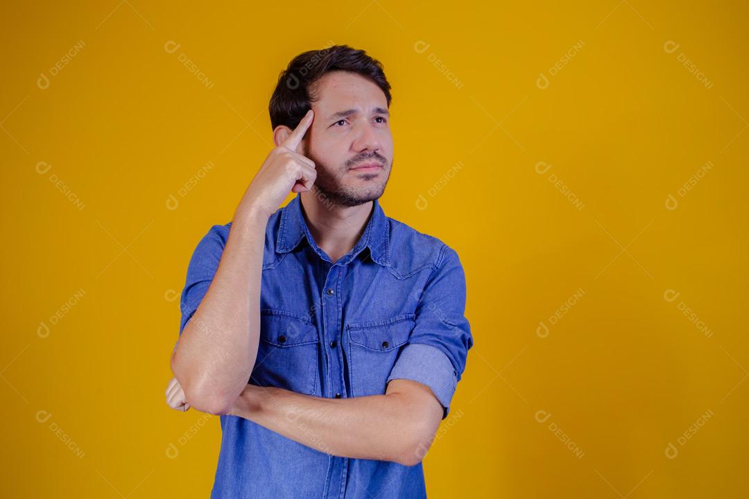 Homem com camisa jeans e braços abertos em fundo amarelo