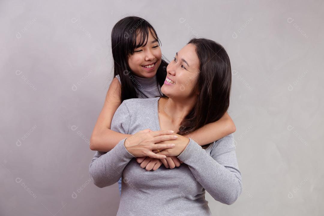 Mãe e filha abraçadas com camisetas cinzas em fundo bege